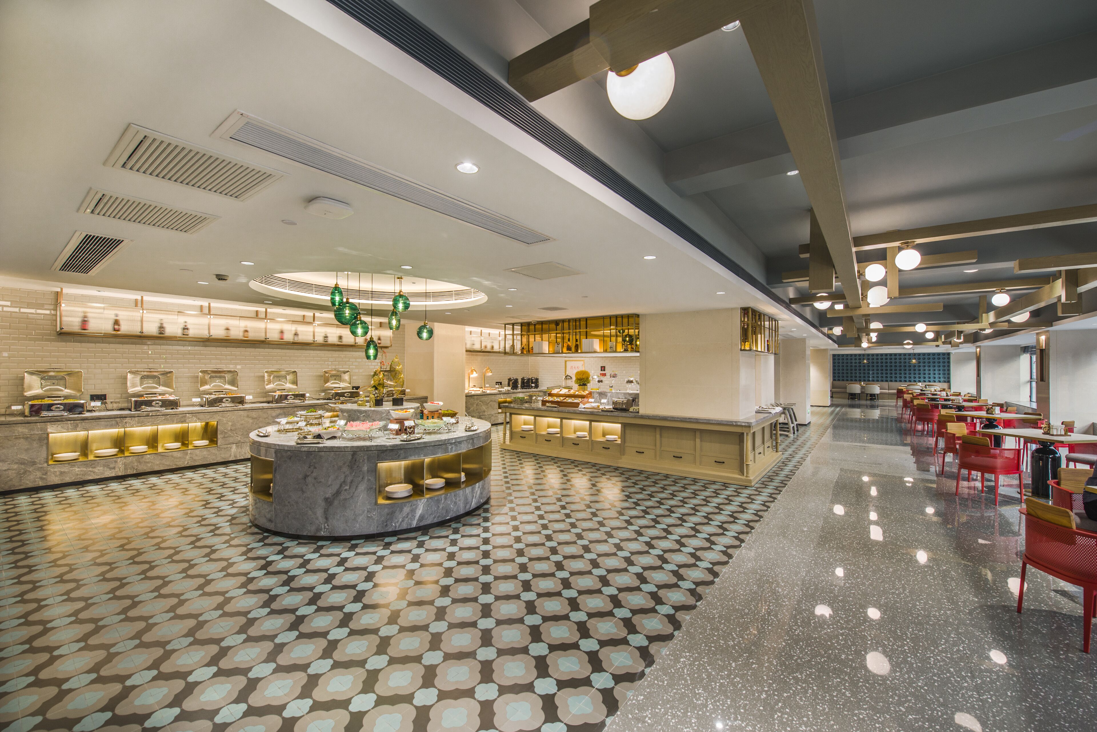 Un espacioso vestíbulo de hotel con una barra circular central, piso con estampado y una amplia zona de comedor con sillas rojas.