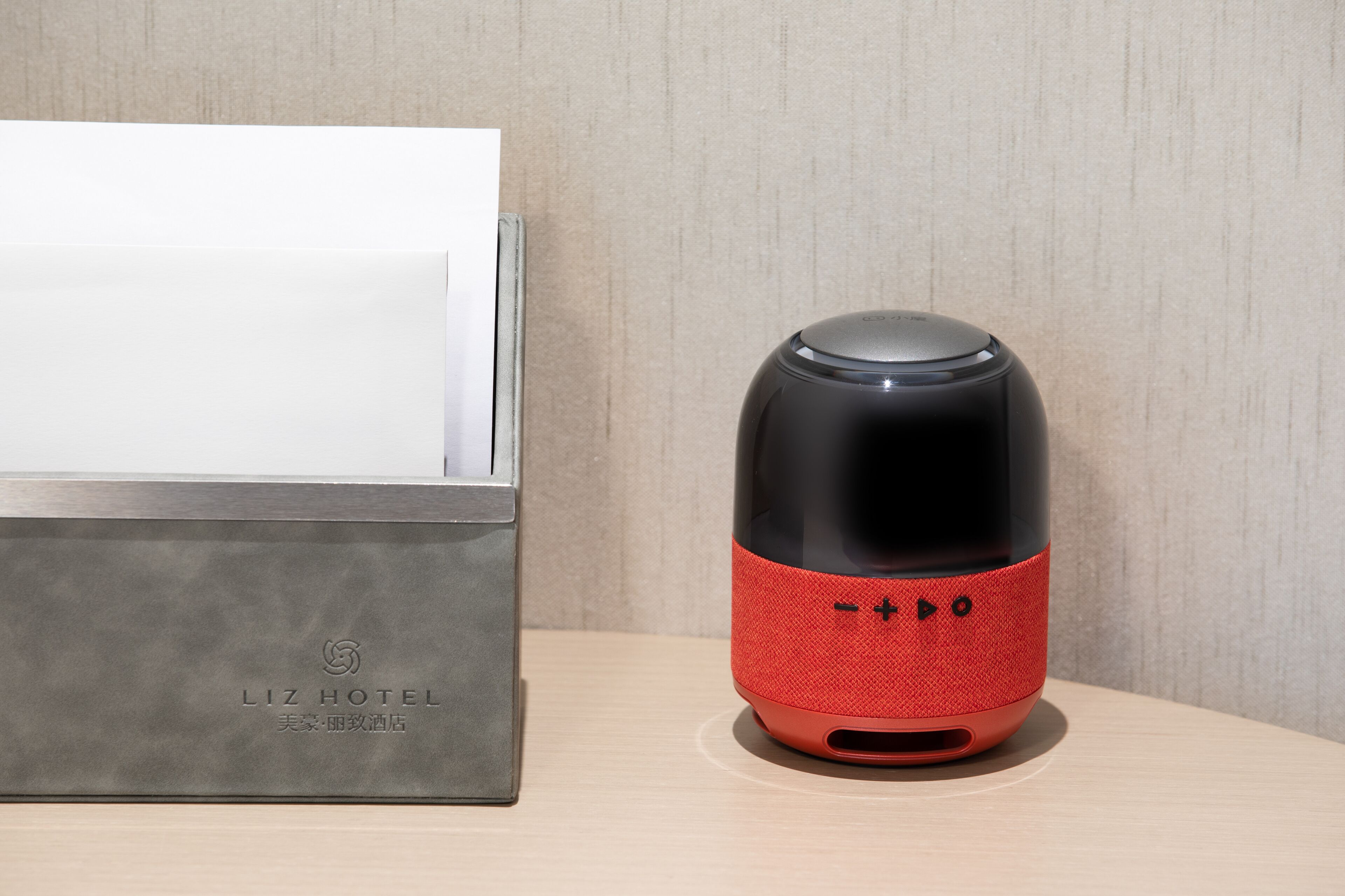 Un altavoz negro y rojo sobre una superficie de madera, junto a una caja metálica con texto en relieve.