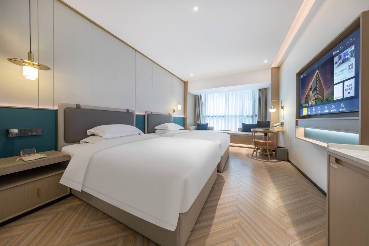 Ett modernt hotellrum med en stor säng, sängbord, ett skrivbord och en tv som är monterad på väggen.
