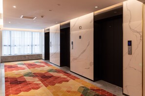A modern elevator area with marble walls, numbered doors, and a colorful geometric carpet. - GZ Baiyun Airport MeHood Liz Hotel T1 (Guangzhou)