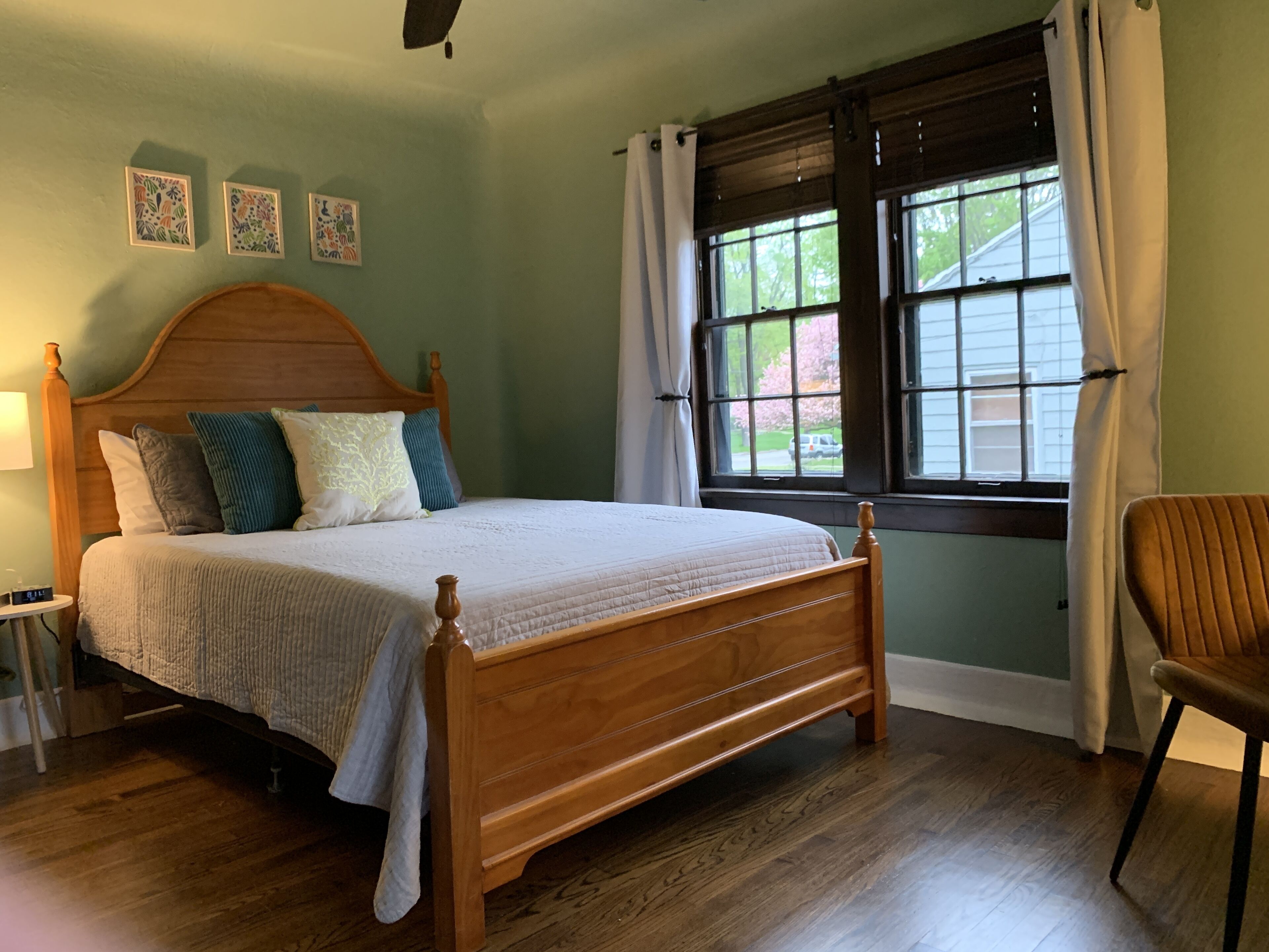 Ein Schlafzimmer mit einem hölzernen Bett, einem Nachttisch, einem Sessel und einem Fenster mit Vorhängen.