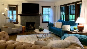 A living room with a fireplace, a blue sofa, a beige armchair, and a coffee table. - HOT TUB | Decked Out Oasis | Nespresso Coffee Bar (South Bend)