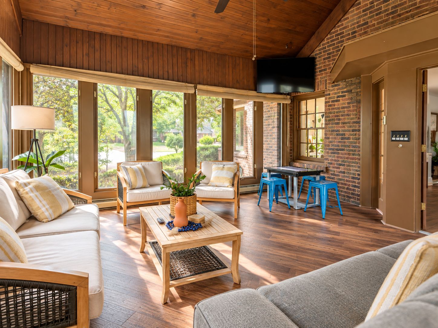 A spacious living area with a wooden ceiling, large windows, a sofa, a coffee table, and a television.