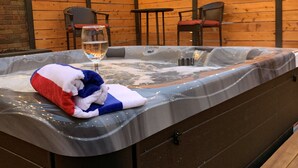 A hot tub with a blanket and a glass of wine, surrounded by wooden walls and string lights. - HOT TUB | Decked Out Oasis | Nespresso Coffee Bar (South Bend)