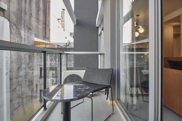 A balcony with a round table and a cushioned bench, overlooking a cityscape.