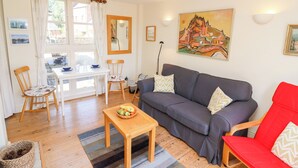 Een gezellige woonkamer met een grijze bank, een rode fauteuil, een houten salontafel en een eettafel met stoelen.