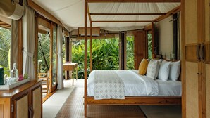 A spacious bedroom with a large bed, wooden furniture, and a view of lush greenery outside. - Nadi Nature Resort - Adults Only (Penebel)