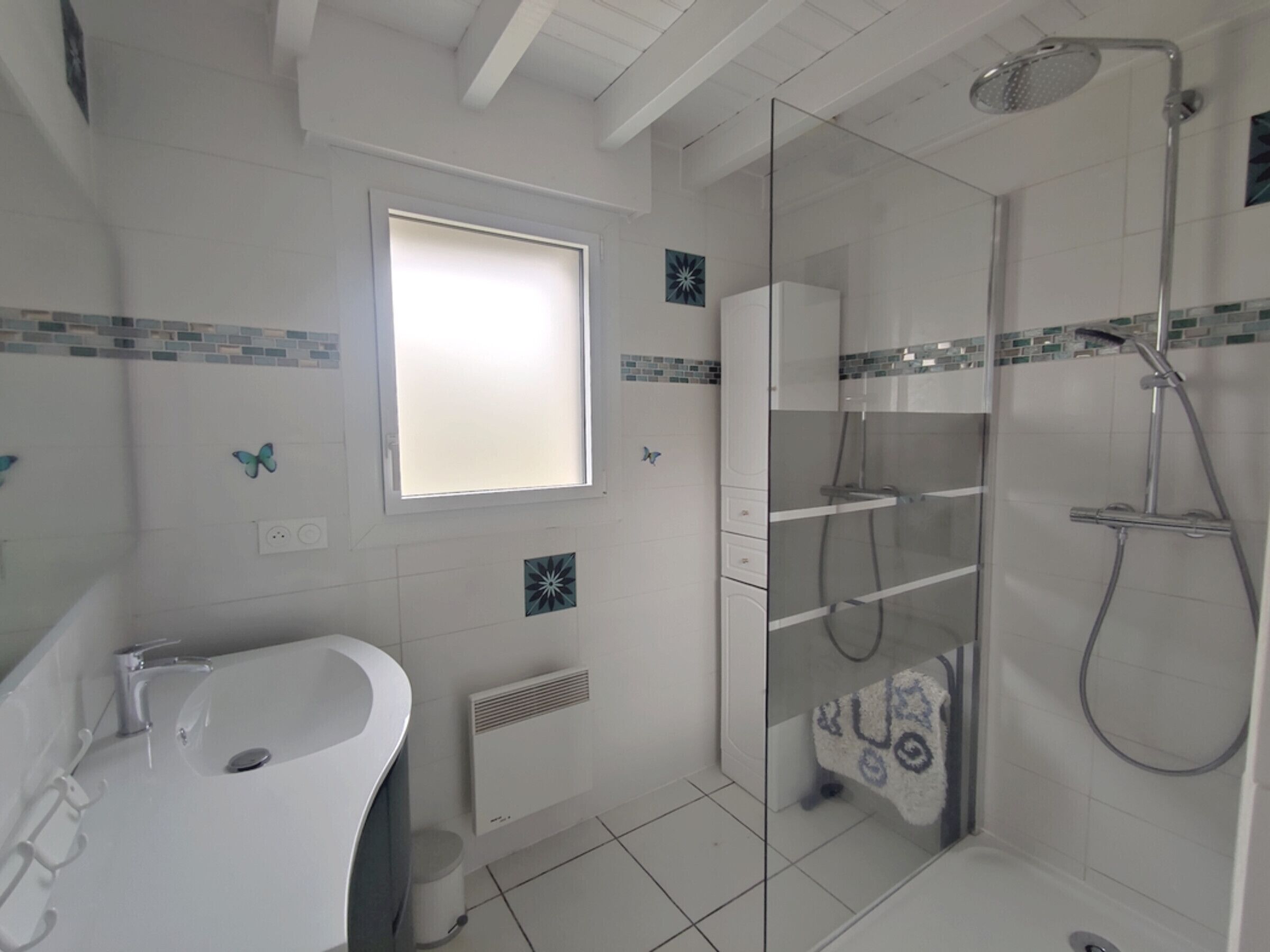 Un baño con cabina de ducha de vidrio, un lavabo blanco y una ventana.