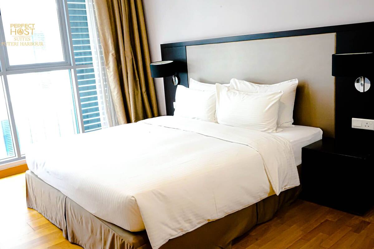A hotel room with a large bed, a nightstand, a wall-mounted lamp, and a window with curtains.