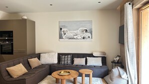 A modern living room with a grey sectional sofa, two wooden side tables, a white rug, and a painting of a polar bear on the wall.
