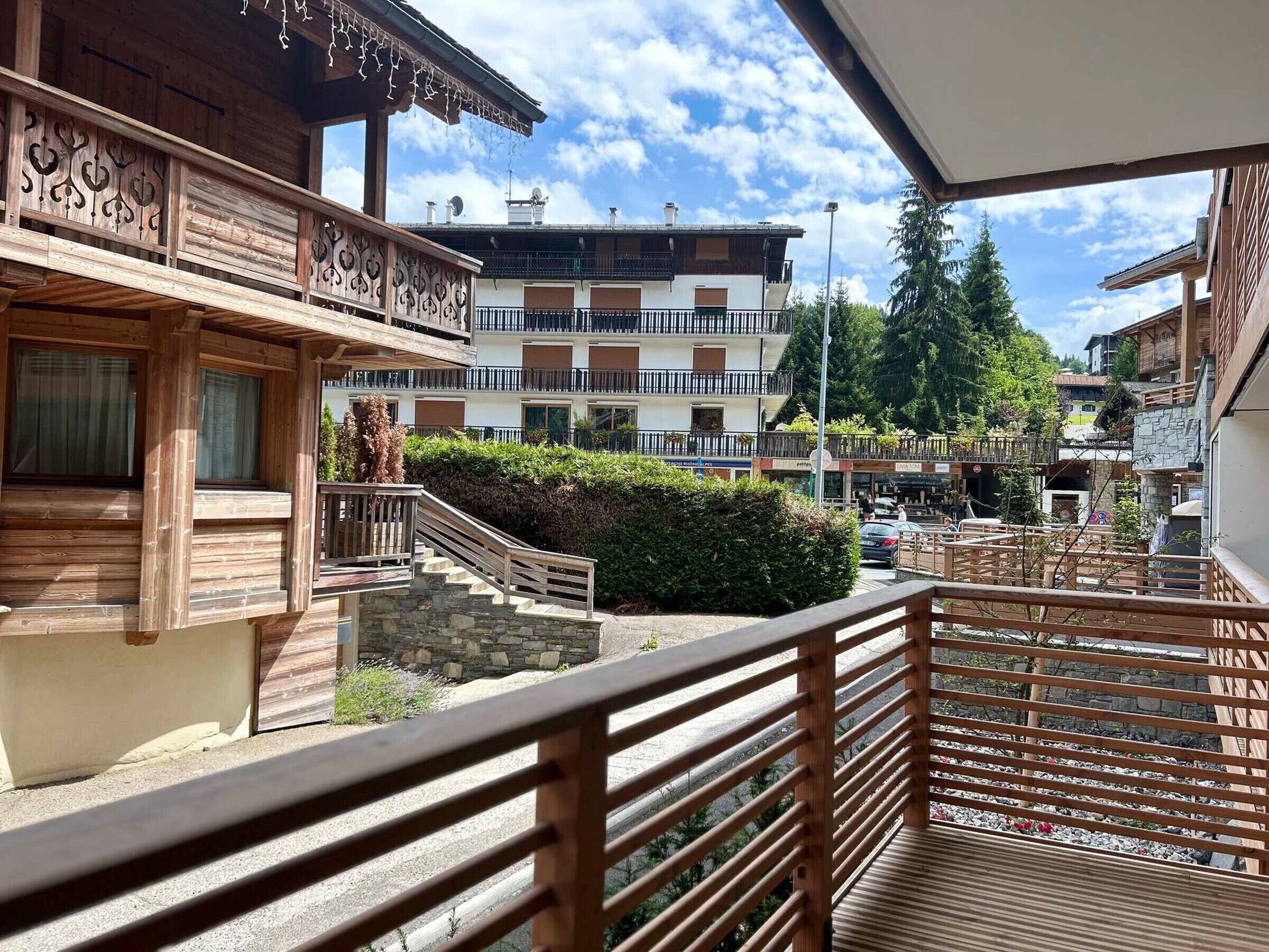 Un balcón de madera con un muro de piedra y vistas a una plaza del pueblo.