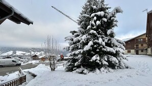 A snow-covered landscape with a large evergreen tree, a building with balconies, and a parked van. - Cozy Studio Cabin for 4 in Crest-Voland, 100m from Ski Lifts and Village, Parking Included (Crest-Voland)
