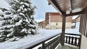 A wooden balcony with a railing, a snow-covered tree, and a building with a balcony in the background. - Cozy Studio Cabin for 4 in Crest-Voland, 100m from Ski Lifts and Village, Parking Included (Crest-Voland)