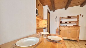 A wooden dining table with plates, glasses, and cutlery, set in a room with wooden cabinets and a tiled backsplash. - Cozy Studio Cabin for 4 in Crest-Voland, 100m from Ski Lifts and Village, Parking Included (Crest-Voland)