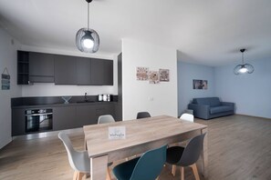 A modern kitchen with dark cabinets, a built-in oven, and a dining area with a wooden table and chairs. - WePuglia - LOI20 - Apt Levante (Monopoli)