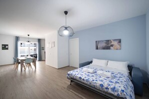 A bedroom with a bed, a desk with chairs, a dining area, and a hallway.