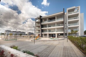 A modern multi-story building with balconies, a playground, and a paved area.