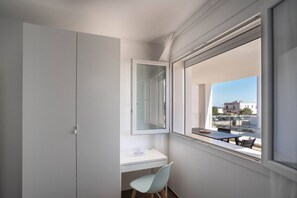 A modern room with a white desk, a chair, a large window, and a wardrobe.
