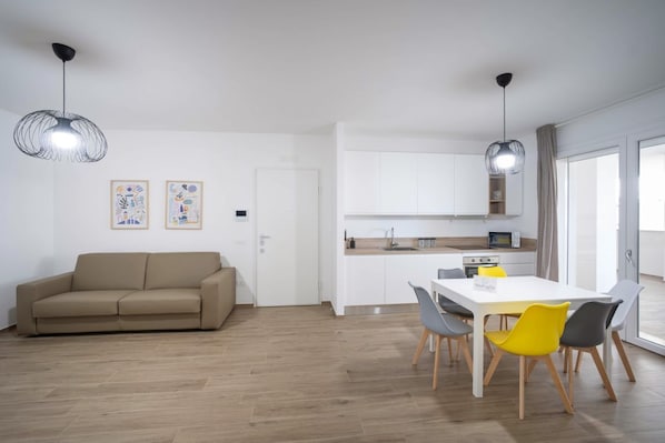 A modern apartment with a sofa, dining table, chairs, kitchen area, and artwork on the wall.