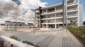 A modern multi-story building with balconies, a playground, and a paved area. - WePuglia - LOI20 - Apt Maestrale (Monopoli)