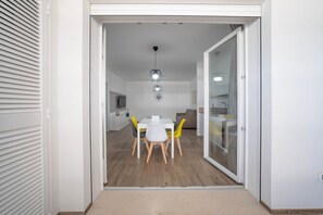 Ein modernes Interieur mit Essbereich, einem weißen Tisch und gelben Stühlen, einer Küche mit Glastür sowie einer Deckenleuchte.