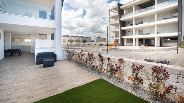 A modern building with multiple floors, outdoor seating area, and a children's play area. - WePuglia - LOI20 - Apt Maestrale (Monopoli)