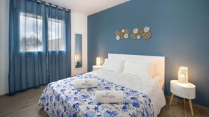 A bedroom with a bed, two bedside tables, a nightstand, a window with curtains, and wall decor. - WePuglia - LOI20 - Apt Maestrale (Monopoli)