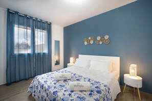 Une chambre à coucher comprenant un lit, deux tables de chevet, une commode, une fenêtre avec des rideaux et des éléments de décoration murale.