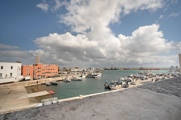 Un port de plaisance avec des bateaux amarrés, un bâtiment doté de nombreuses fenêtres et un grand navire en arrière-plan.