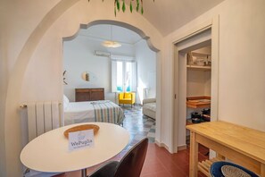 Hotellihuone, jossa on sänky, ruokapöytä, tuoli, pieni pöytä, jossa on kori, keltainen tuoli, ikkuna ja keittiöalue.