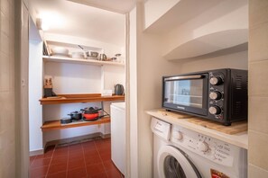 Kompakti keittiö, jossa on mikroaaltouuni, pesukone ja hyllyjä keittiötarvikkeille.