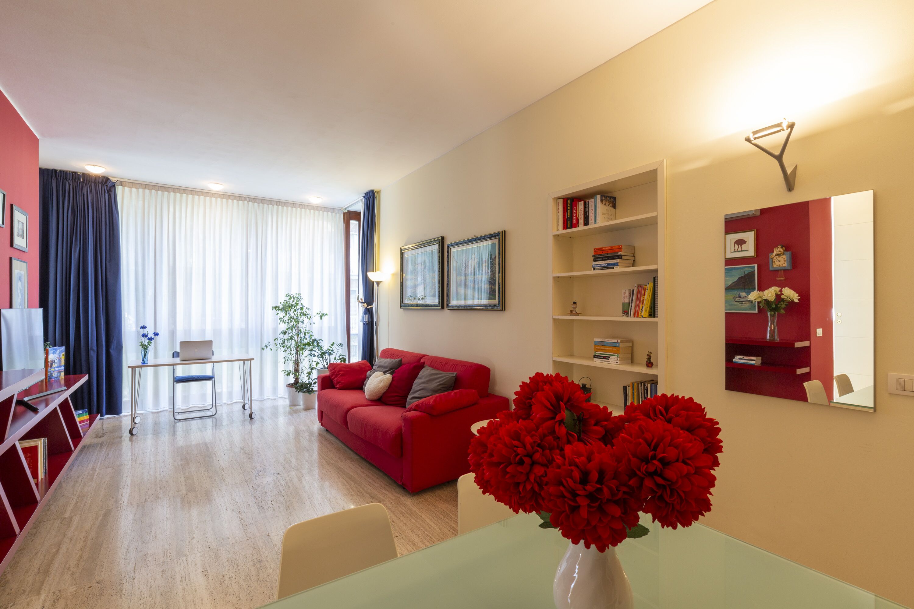 A modern living room with a red sofa, a glass coffee table, and a bookshelf.