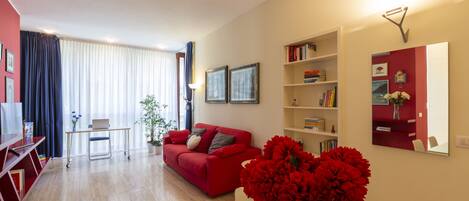 A modern living room with a red sofa, a glass coffee table, and a bookshelf.