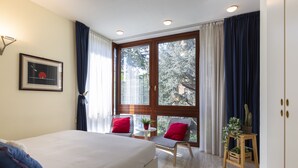 A bedroom with a large bed, two chairs, a small table with a plant, and a window with curtains. - notaMI - Twins Apartment  (Milan)