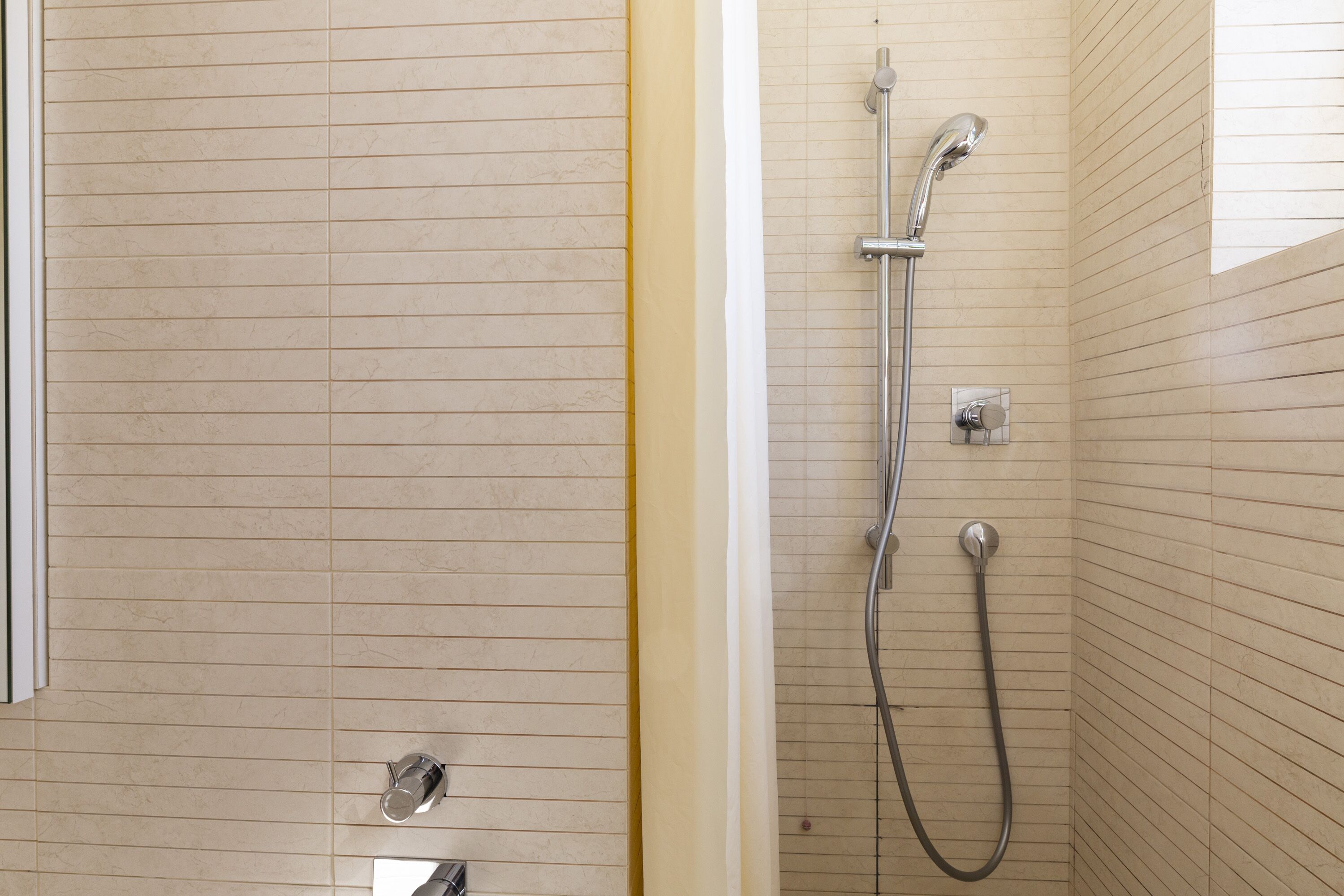Un bagno con pareti piastrellate, una doccia con soffione manuale e un rubinetto a parete.