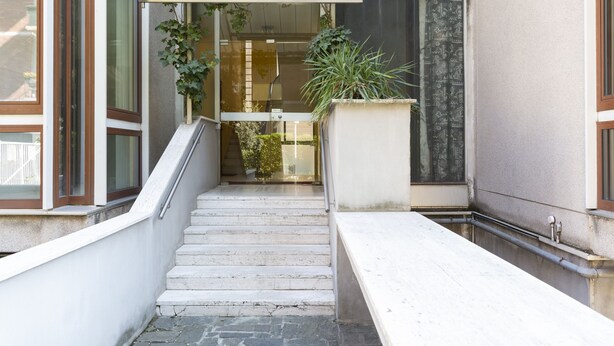 A staircase leading to a building entrance with a bench, potted plants, and a glass door. - notaMI - Twins Apartment  (Milan)