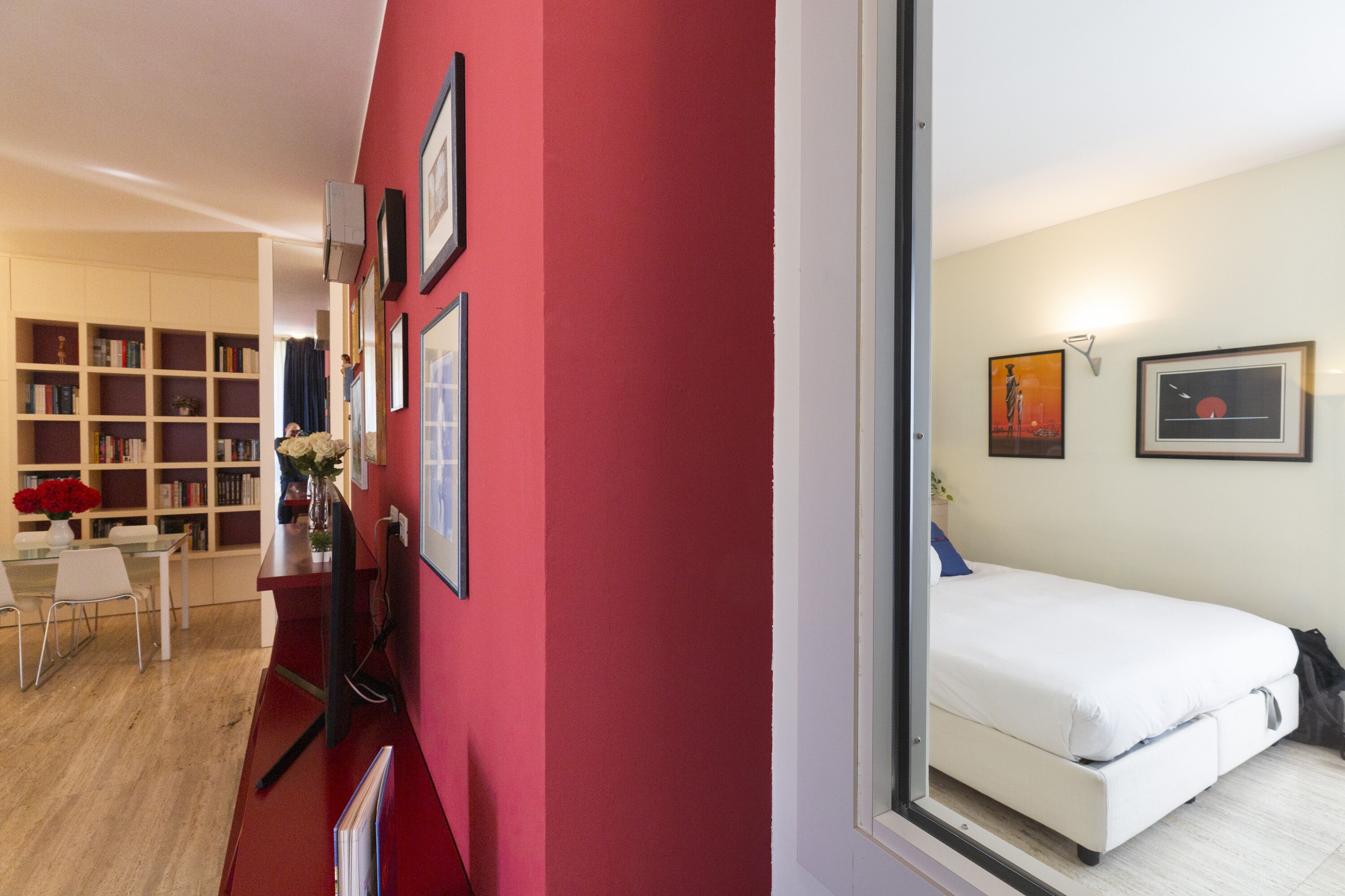 A room with a red accent wall, a white bed, and a bookshelf filled with books.