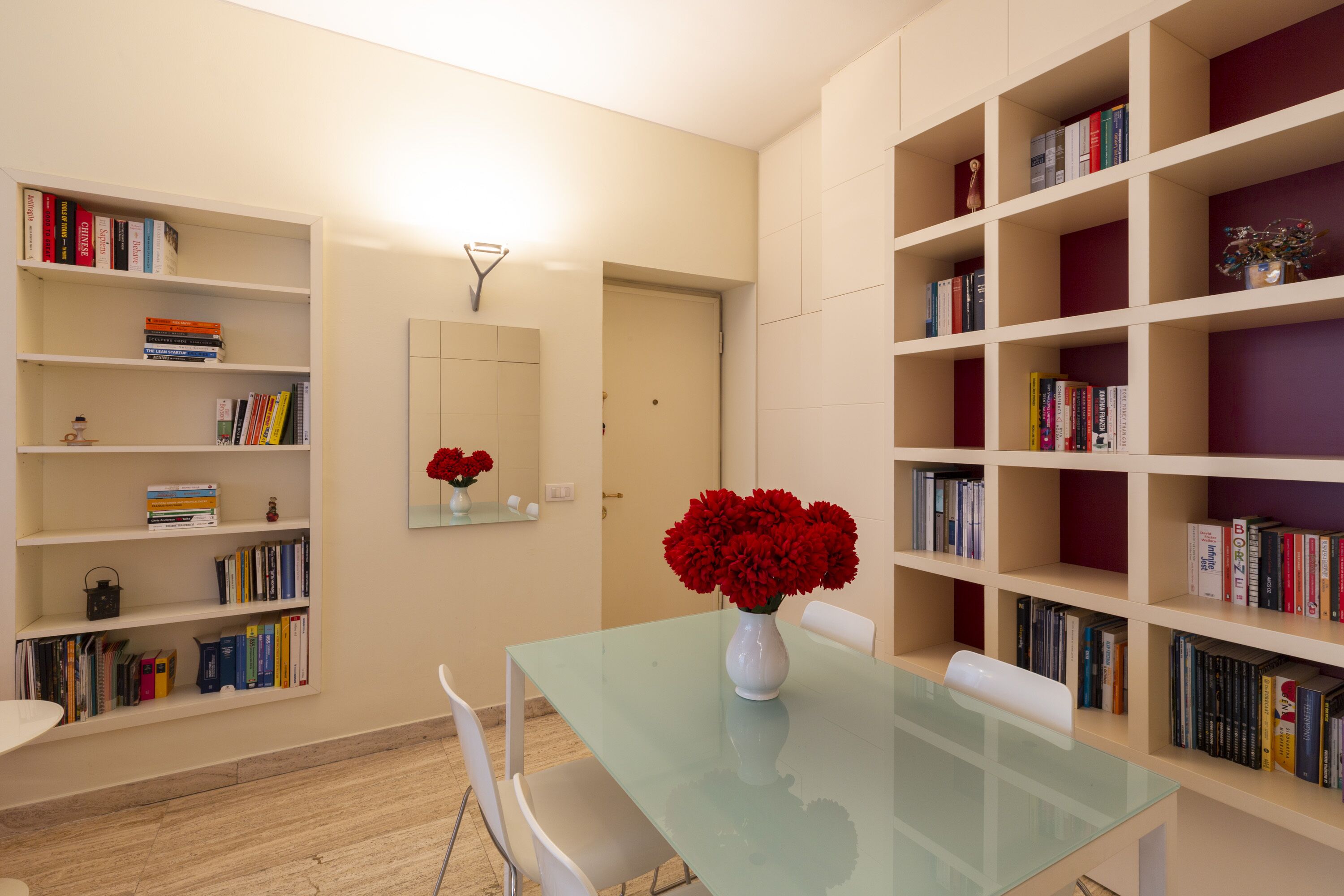 Et moderne bibliotek med bogreoler, et glasbord og hvide stole.