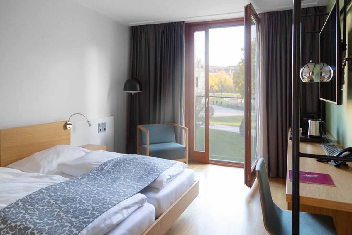 A hotel room with a bed, a desk, a chair, and a view of the outdoors.