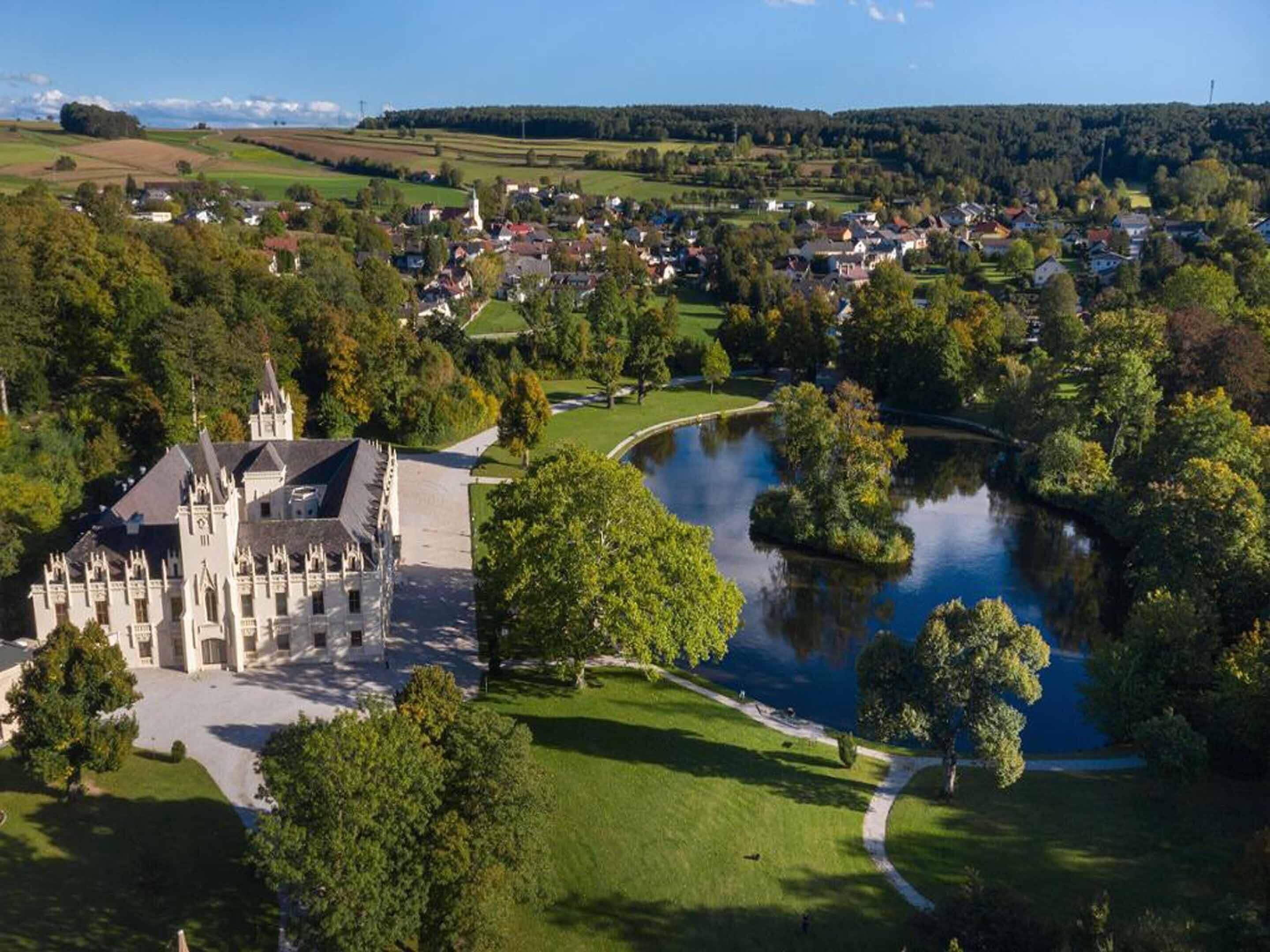 A castle with a large courtyard, a lake, and surrounding greenery.