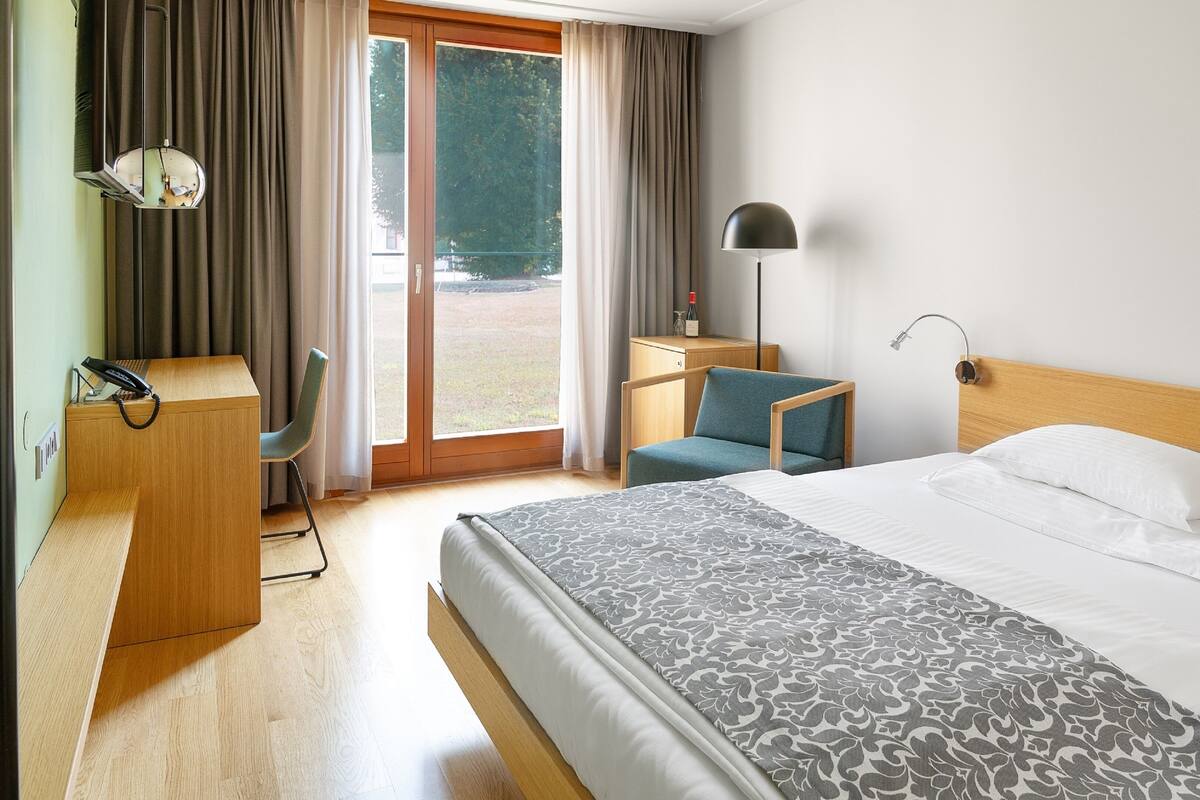 A hotel room with a bed, desk, chair, and a view of the outdoors.