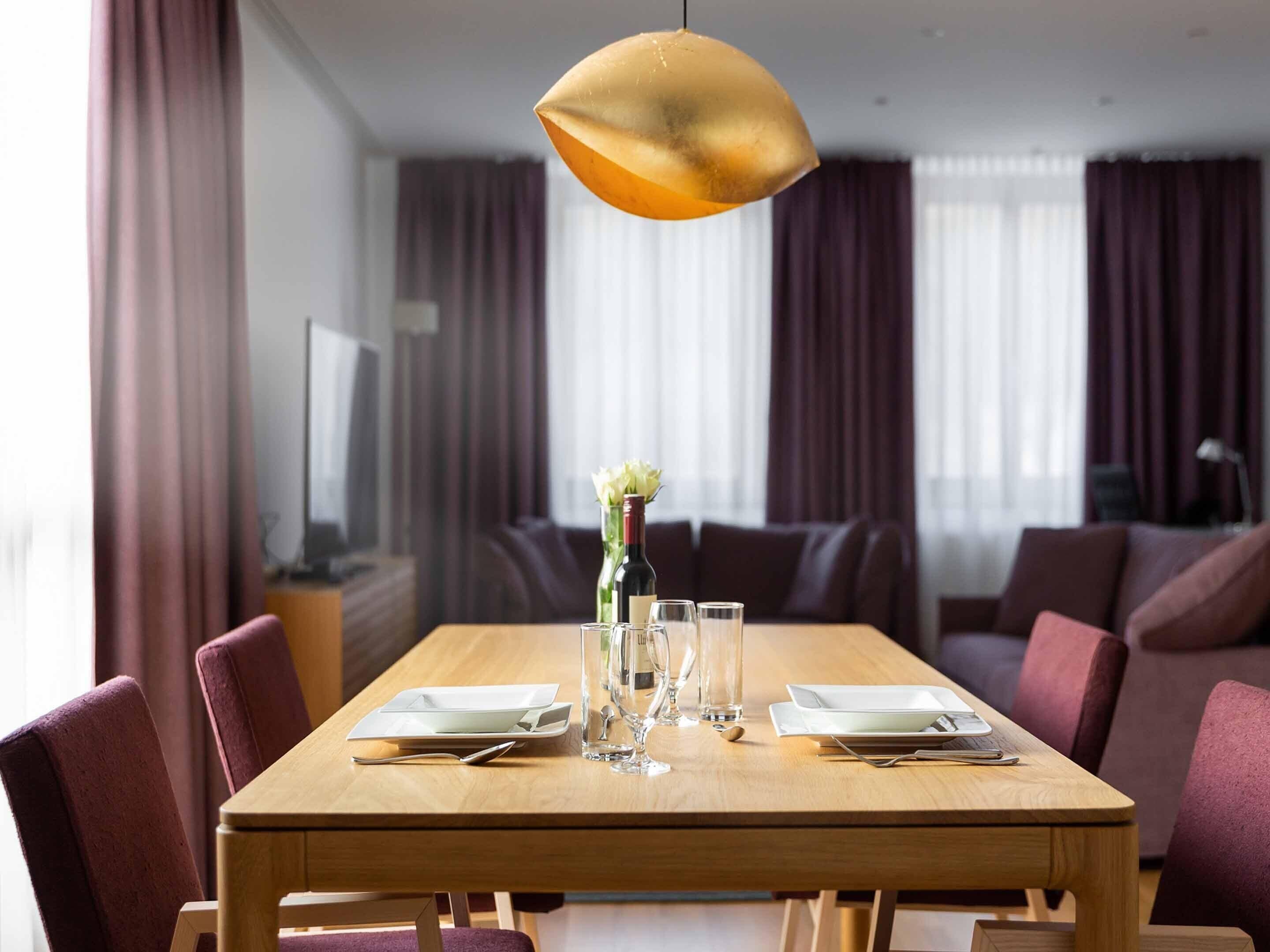 A dining area with a wooden table set for four, a vase with flowers, and a modern pendant light.