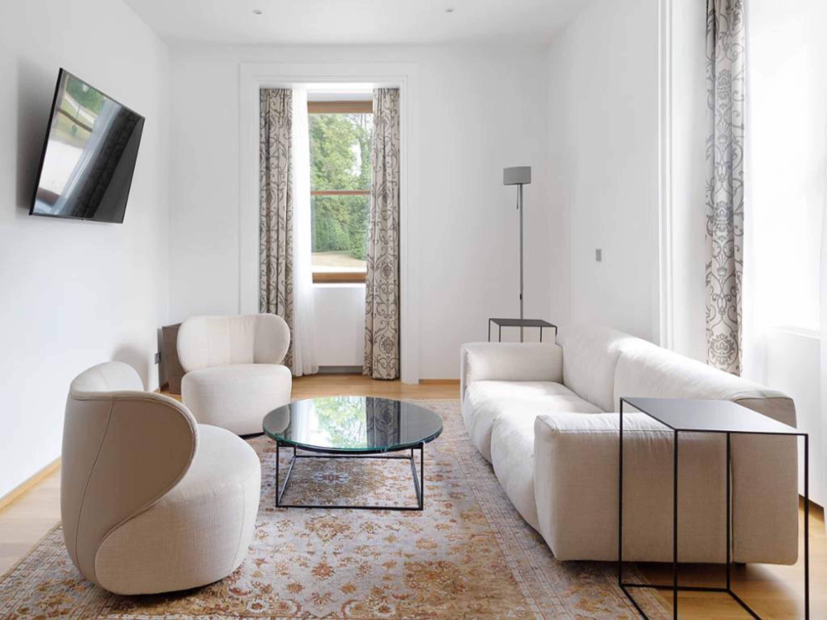 A modern living room with a sofa, armchairs, a glass coffee table, and a floor lamp.