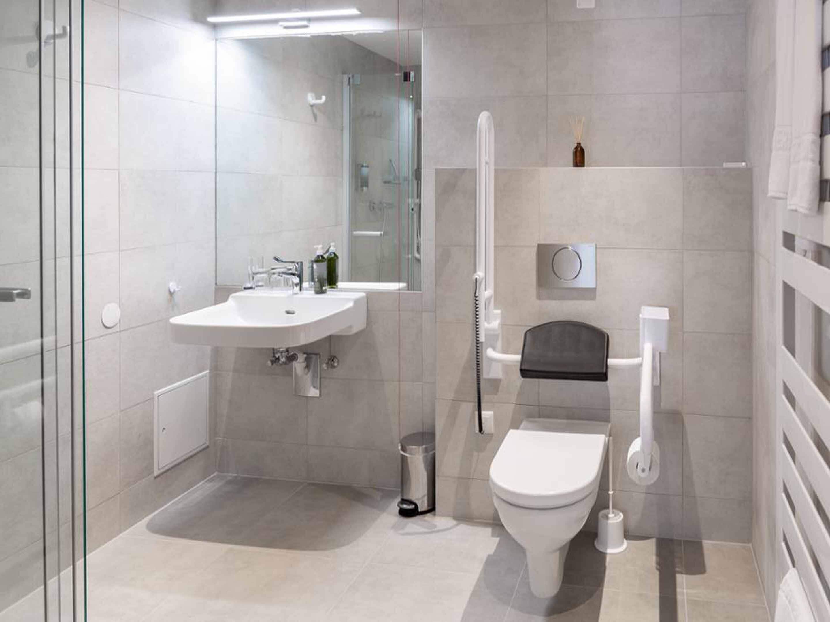 A modern bathroom with a glass shower enclosure, a white sink, a toilet, and a small shelf with a bottle.
