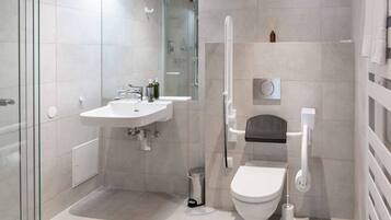 A modern bathroom with a glass shower enclosure, a white sink, a toilet, and a small shelf with a bottle.