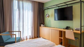 Una habitación de hotel con dos camas, un escritorio con una silla, un televisor y una ventana con cortinas.