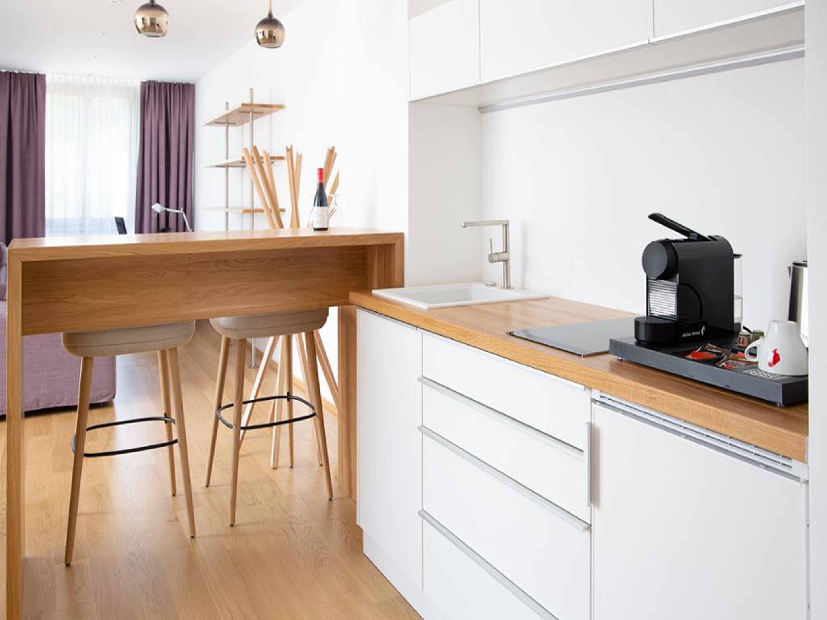 A modern kitchen with a wooden countertop, two bar stools, a coffee machine, and a sink.