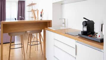 A modern kitchen with a wooden countertop, two bar stools, a coffee machine, and a sink.