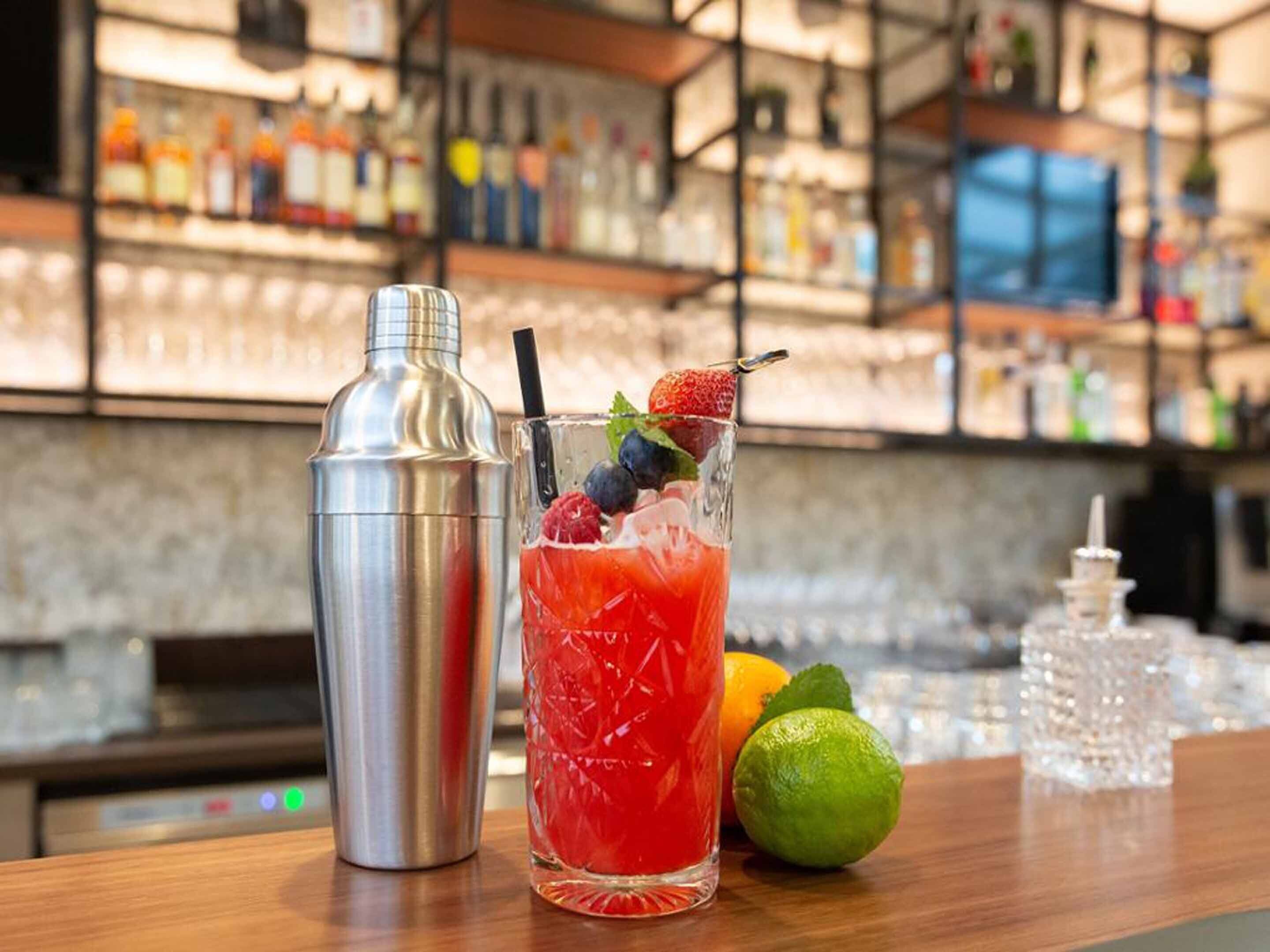Um cocktail com morango, lima e folha de menta sobre um balcão de bar.