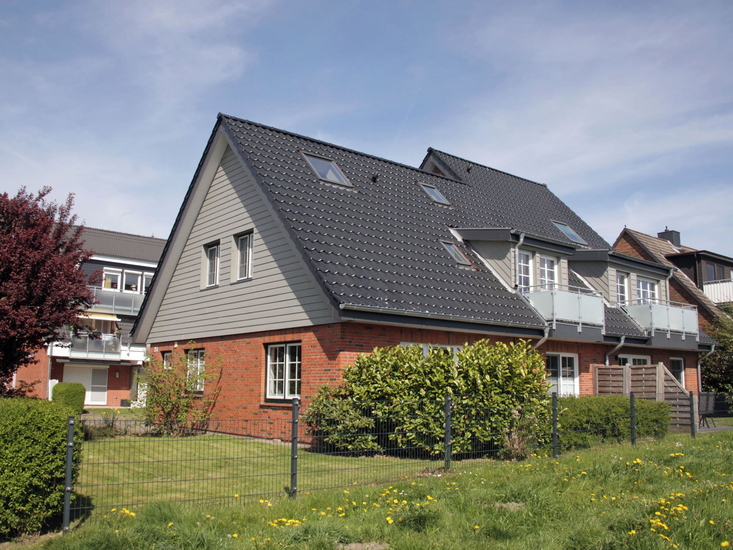 A residential house with a sloped roof, a brick facade, and a fenced yard with yellow flowers.